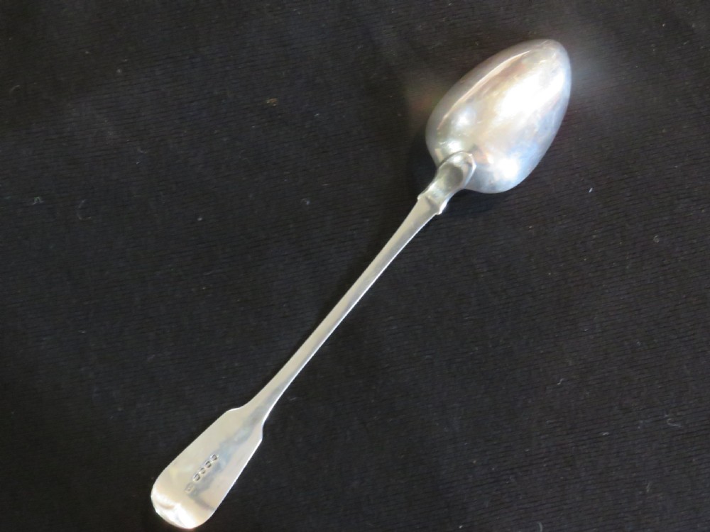 A George III sterling silver basting spoon featuring a plain handle stamped with British hallmarks and a deep oval bowl.