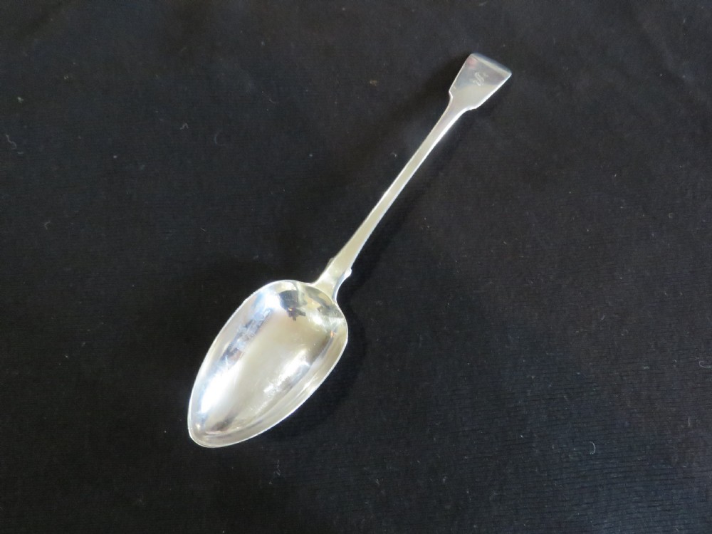 A George III sterling silver basting spoon featuring a plain handle stamped with British hallmarks and a deep oval bowl. View II