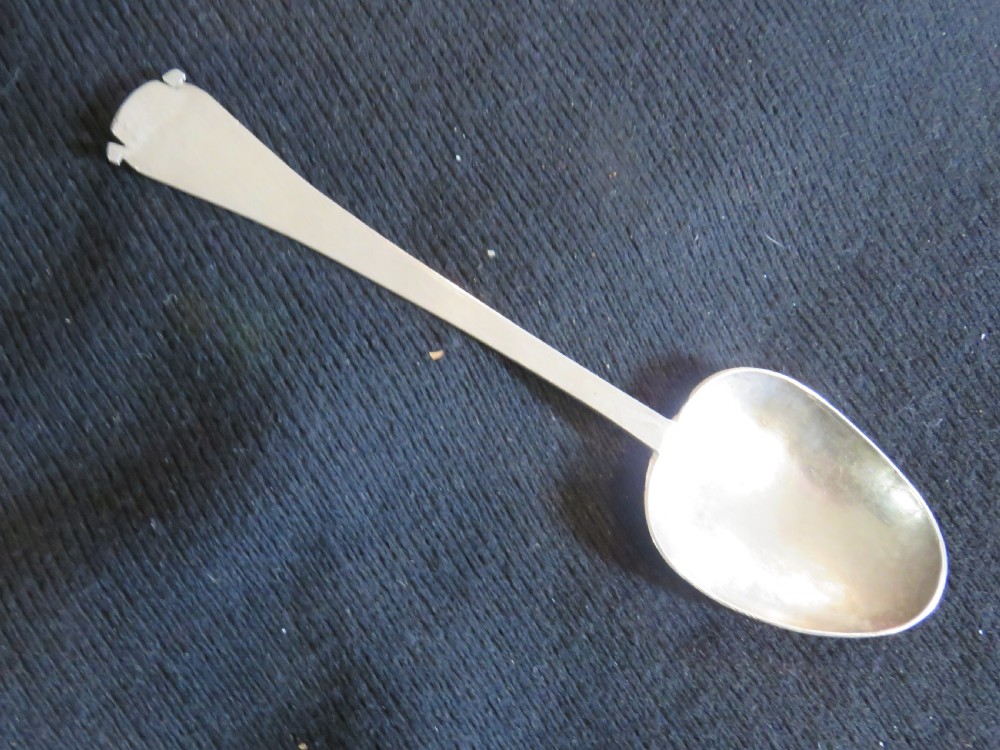 An antique Charles II silver trefid spoon featuring a flat notched handle and an oval bowl set against a dark fabric background.