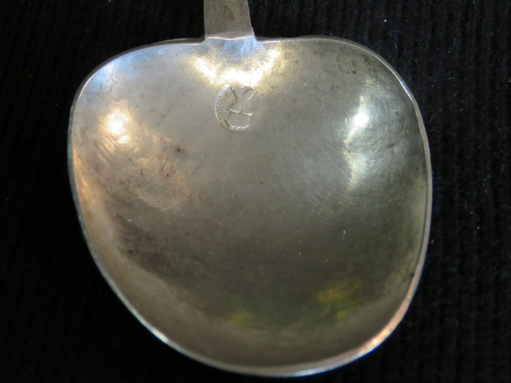 An antique Charles II silver trefid spoon featuring a flat notched handle and an oval bowl set against a dark fabric background. View II