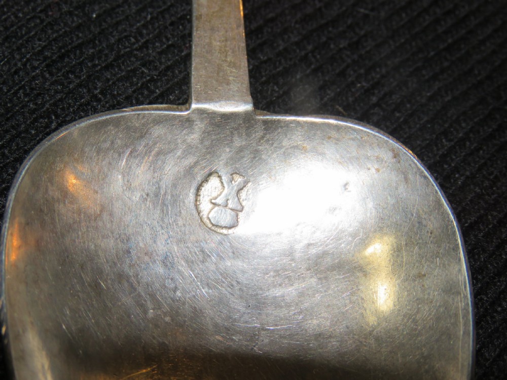 An antique Charles II silver trefid spoon featuring a flat notched handle and an oval bowl set against a dark fabric background. View III