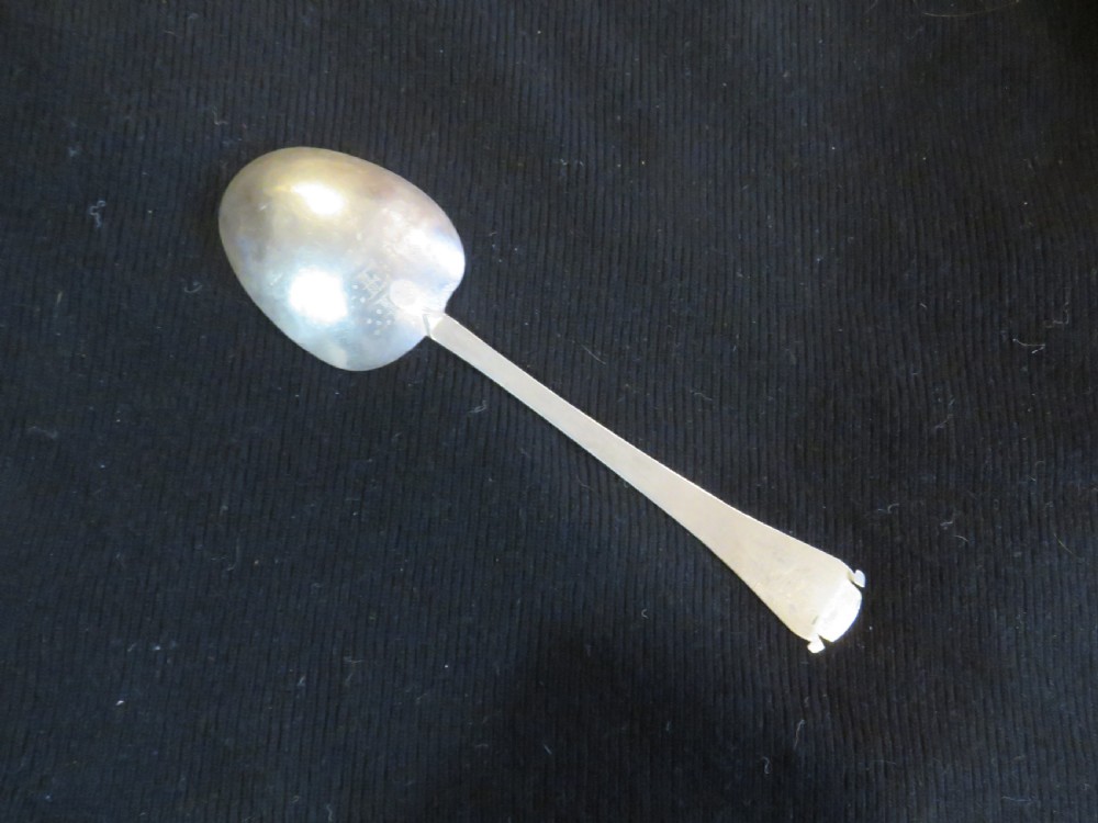 An antique Charles II silver trefid spoon featuring a flat notched handle and an oval bowl set against a dark fabric background. View IV
