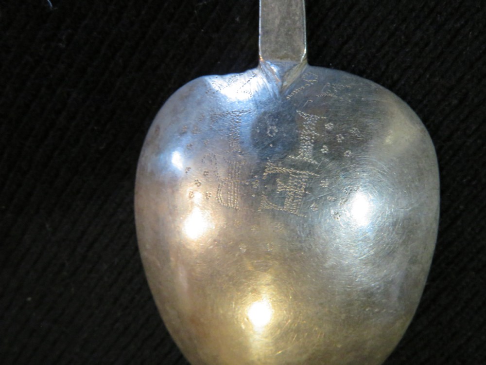 An antique Charles II silver trefid spoon featuring a flat notched handle and an oval bowl set against a dark fabric background. View V