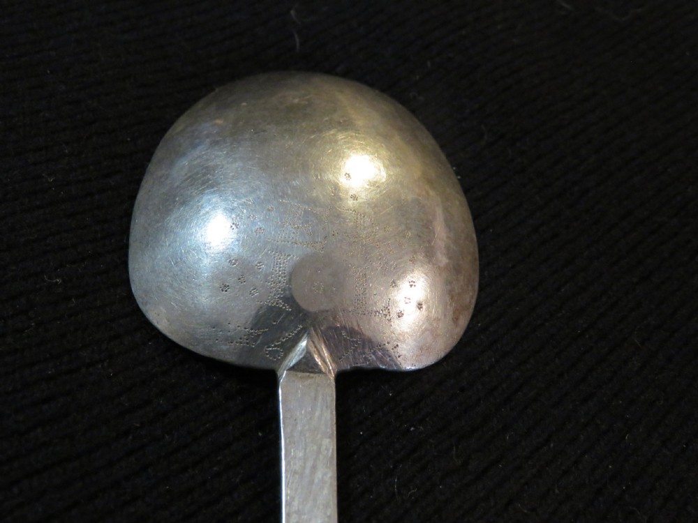 An antique Charles II silver trefid spoon featuring a flat notched handle and an oval bowl set against a dark fabric background. View VI