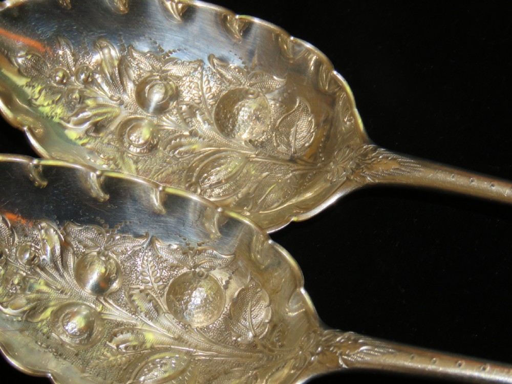 A pair of Georgian sterling silver berry spoons featuring repousse fruit motifs on shaped bowls and detailed engraving along the handles. View II