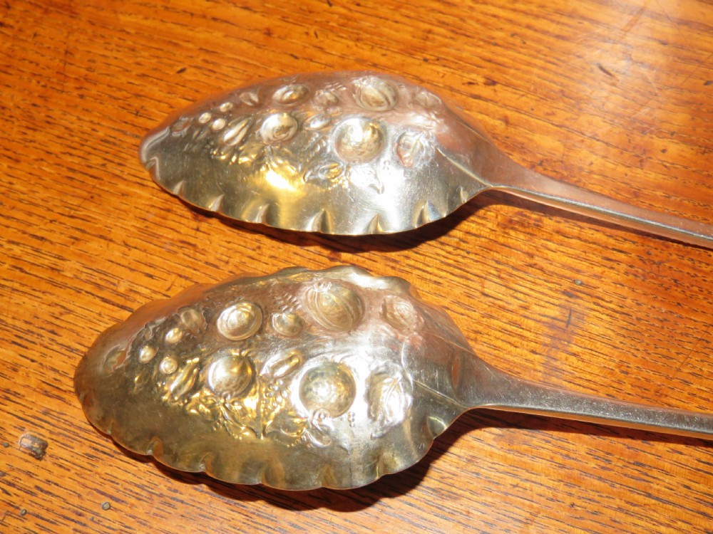 A pair of Georgian sterling silver berry spoons featuring repousse fruit motifs on shaped bowls and detailed engraving along the handles. View V