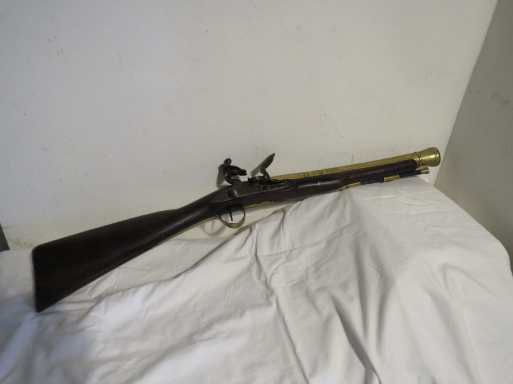 An antique flintlock blunderbuss featuring a flared brass barrel, dark wood stock, iron lock mechanism, and brass trigger guard.