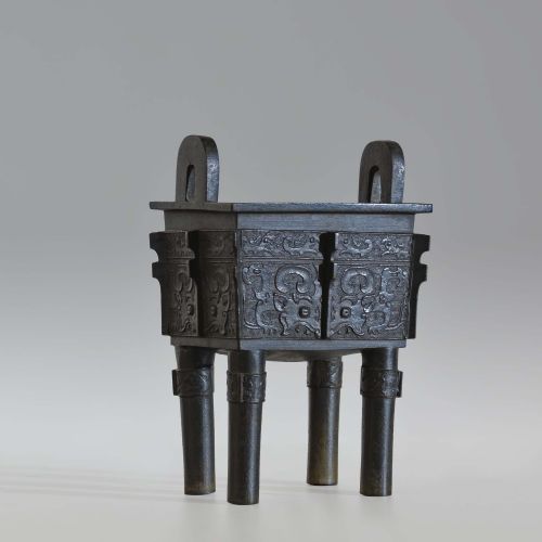 fig 1. A rectangular dark bronze ritual vessel featuring four straight legs, two upright loop handles, relief carvings, and corner flanges.