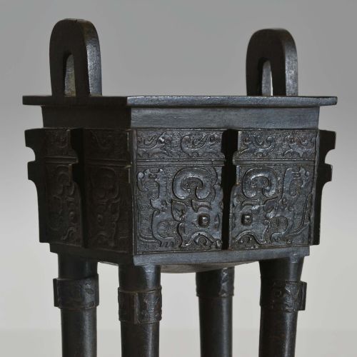 fig 2. A rectangular dark bronze ritual vessel featuring four straight legs, two upright loop handles, relief carvings, and corner flanges.