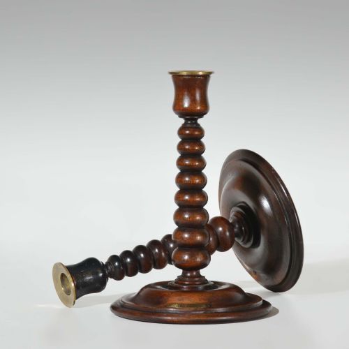 fig 1. A pair of dark turned teak candlesticks featuring repeating bobbin stems, circular bases with small brass plaques, and brass sconce inserts at the top.