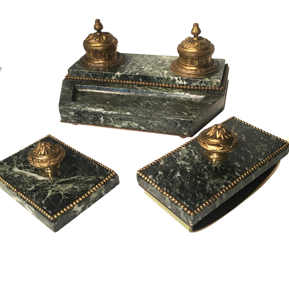 A three-piece antique French green marble desk set with gilt ormolu mounts, comprising a dual-inkwell stand, a rocker blotter, and a matching lidded box.