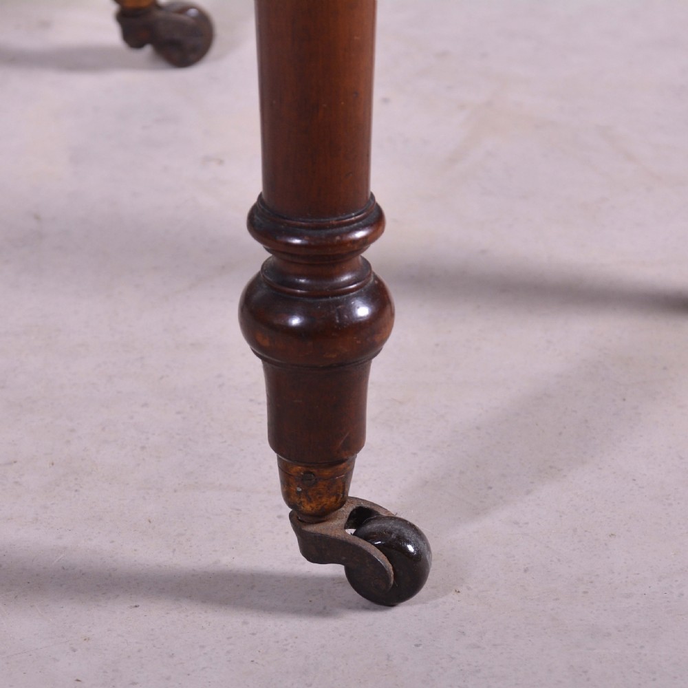 A dark mahogany drop-leaf occasional table featuring a single drawer with two round wooden knobs, four turned legs, and brass castors. View III
