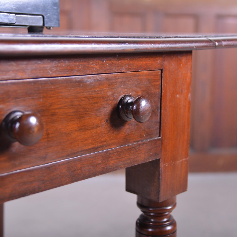 A dark mahogany drop-leaf occasional table featuring a single drawer with two round wooden knobs, four turned legs, and brass castors. View IV
