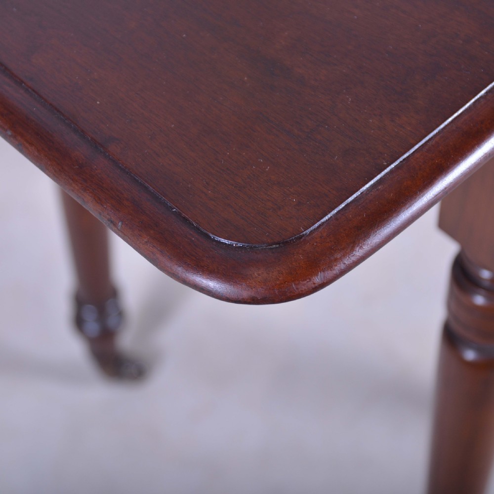 A dark mahogany drop-leaf occasional table featuring a single drawer with two round wooden knobs, four turned legs, and brass castors. View V