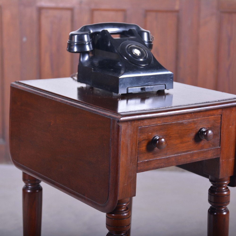 A dark mahogany drop-leaf occasional table featuring a single drawer with two round wooden knobs, four turned legs, and brass castors. View VI