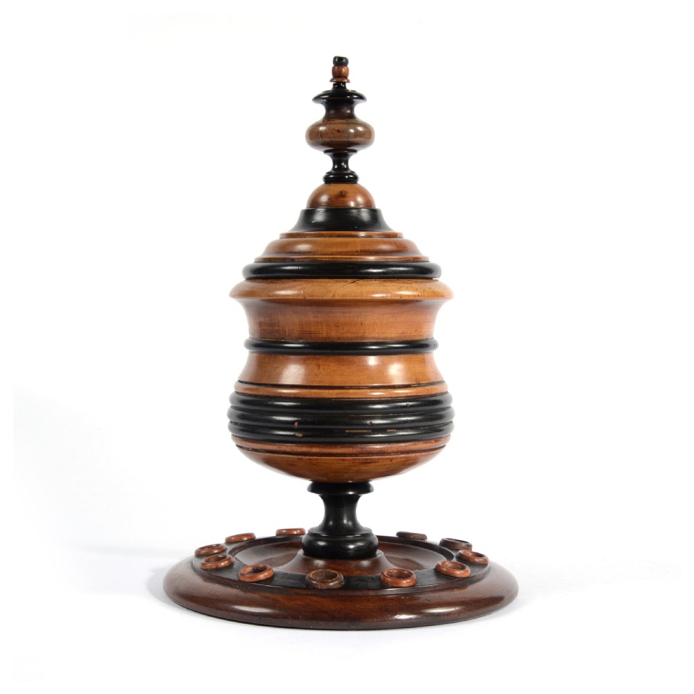 A turned fruitwood tobacco box featuring ebonised ring bands, a tiered lid with a turned finial, and a circular base with pipe holders.