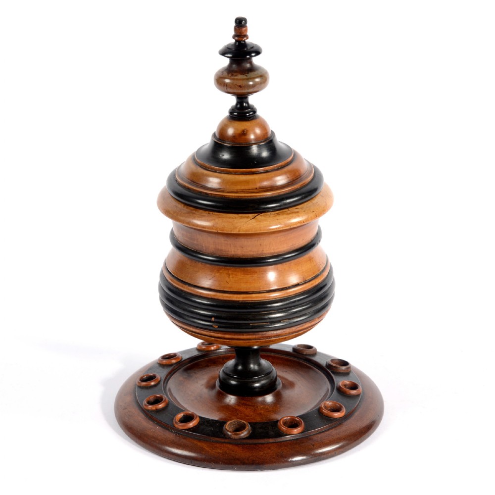 A turned fruitwood tobacco box featuring ebonised ring bands, a tiered lid with a turned finial, and a circular base with pipe holders. View VII