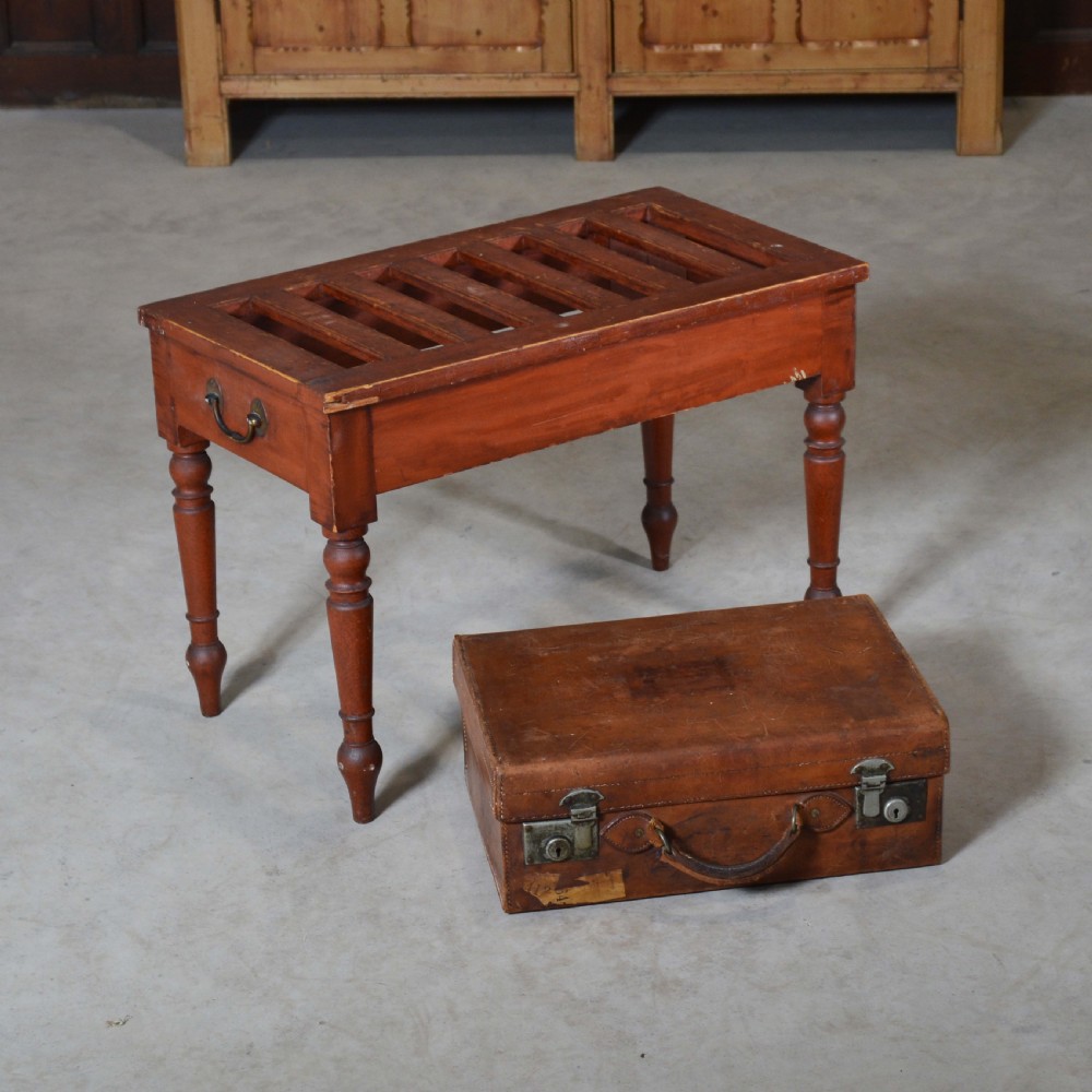 A low rectangular pine luggage stand painted in terracotta red with a slatted top surface, side handles, and four turned legs.