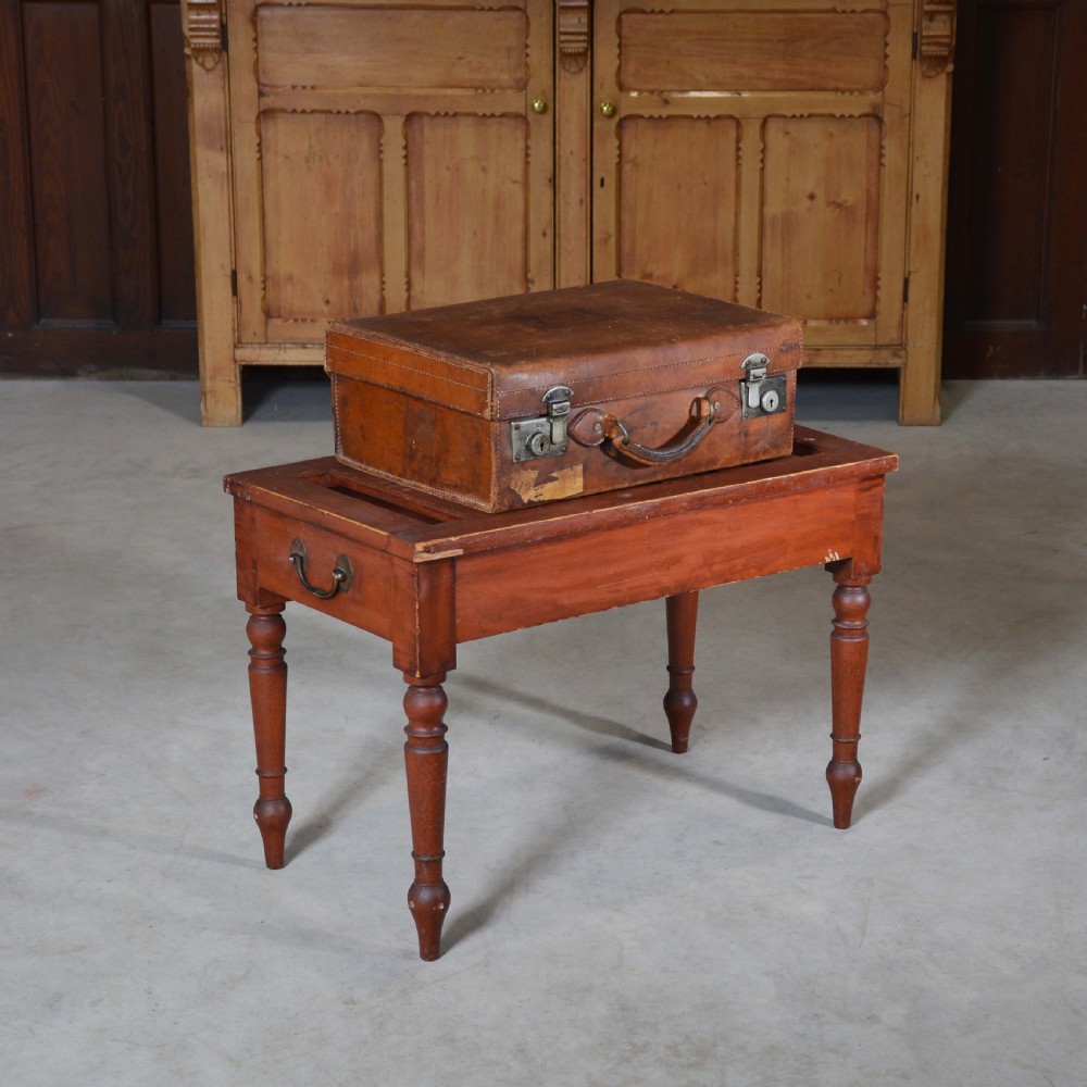 A low rectangular pine luggage stand painted in terracotta red with a slatted top surface, side handles, and four turned legs. View II