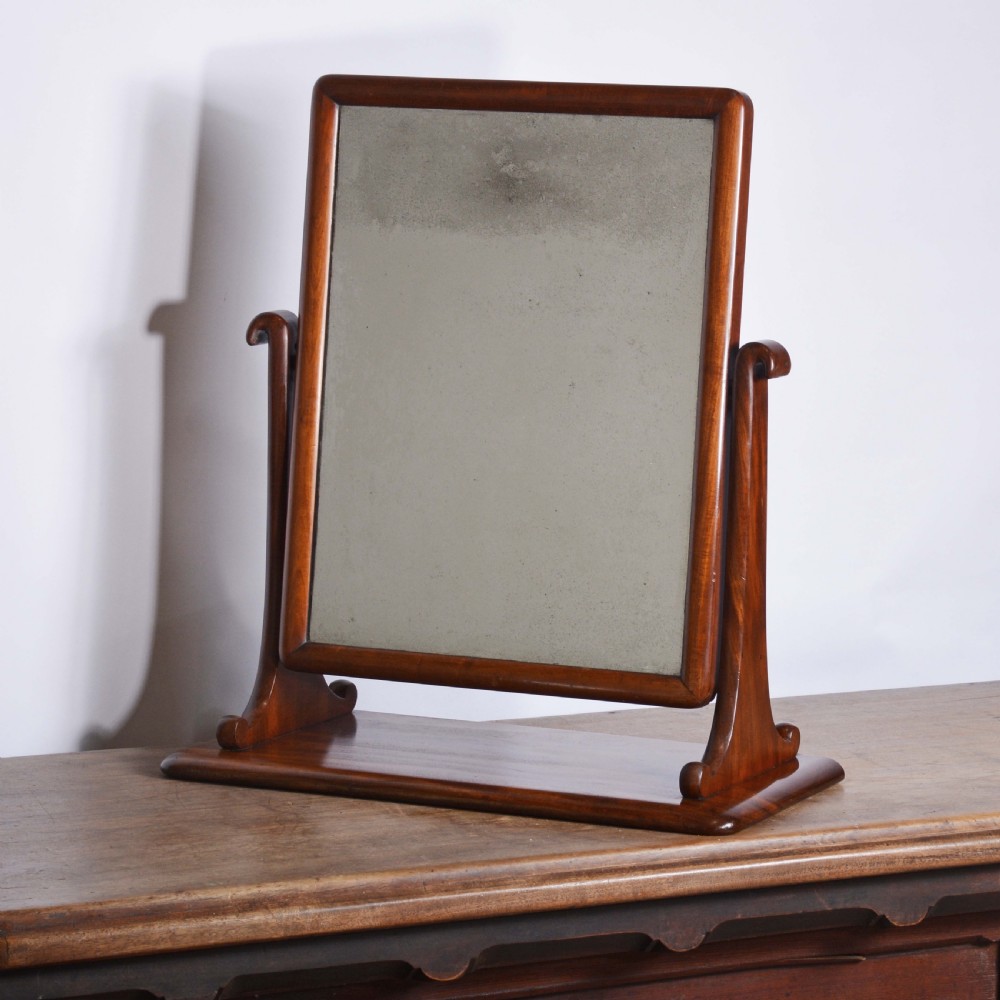 An antique mahogany dressing table mirror featuring a rectangular swivelling frame set between curved upright supports on a solid plinth base.