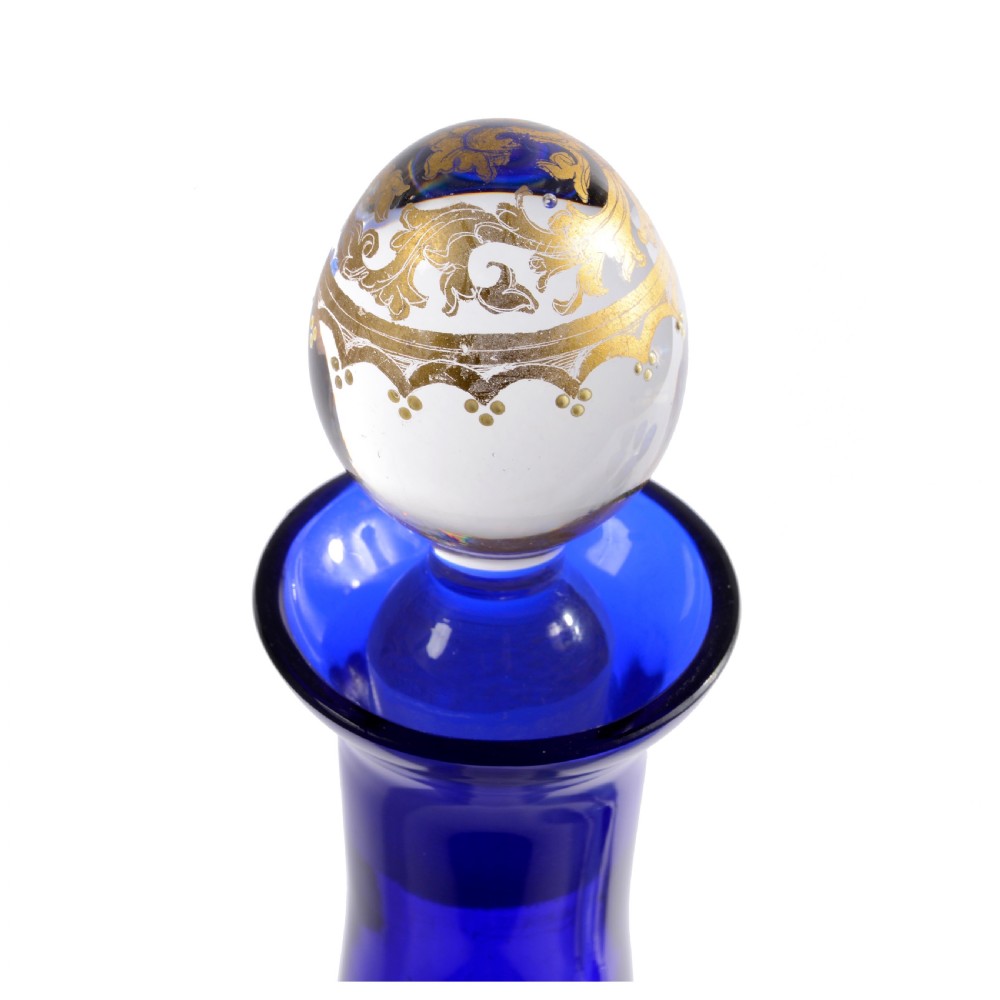 A 19th-century Venetian cobalt blue glass decanter bottle with stopper and matching stemmed glasses featuring gilded classical motifs and clear twisted glass stems. View VI