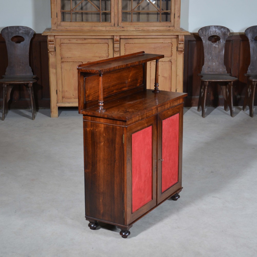 A Regency dwarf rosewood chiffonier featuring two red fabric-lined panel doors, a raised upper shelf supported by turned columns, and bun feet. View II