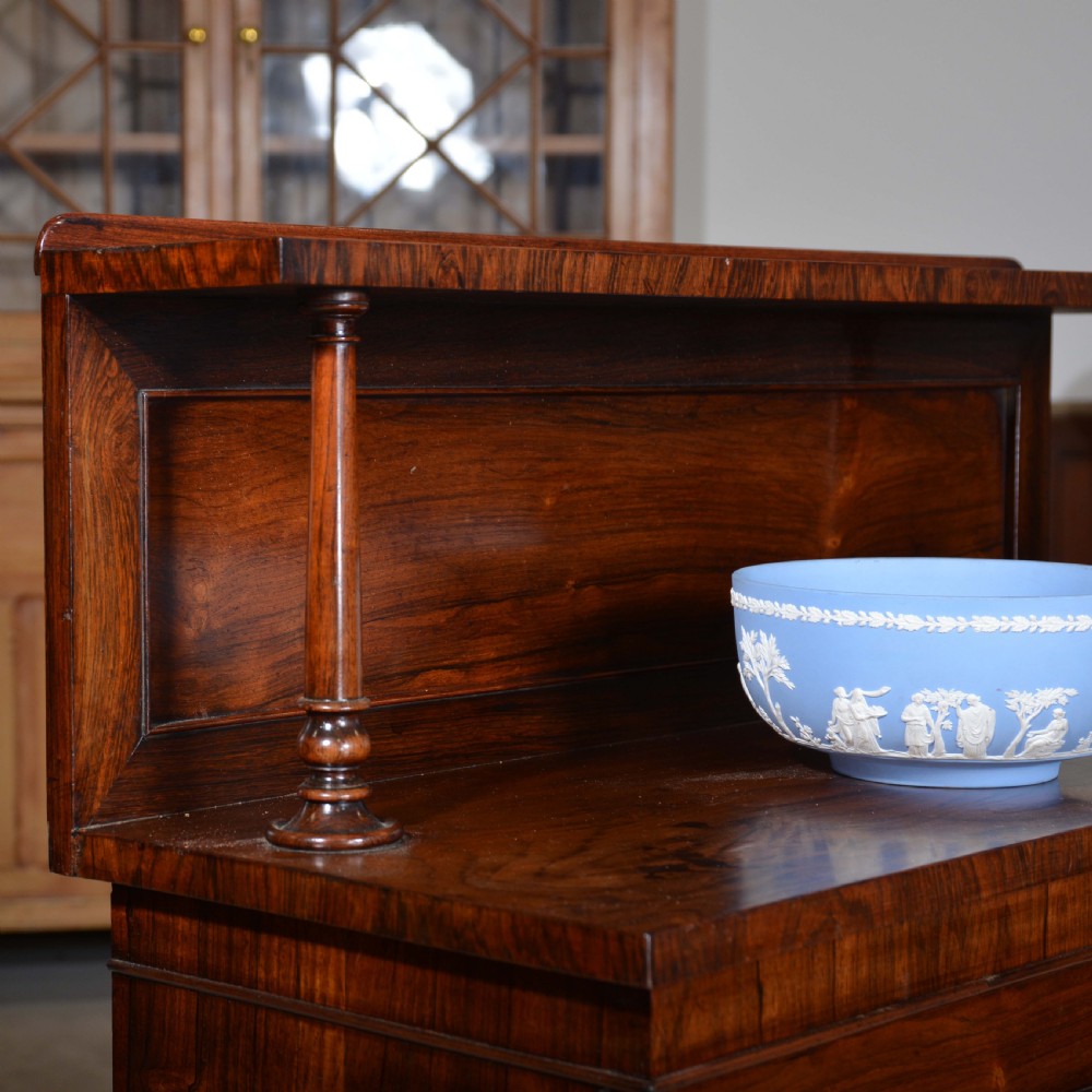 A Regency dwarf rosewood chiffonier featuring two red fabric-lined panel doors, a raised upper shelf supported by turned columns, and bun feet. View VIII