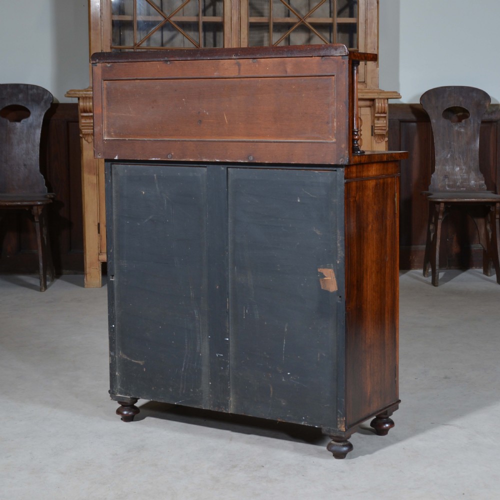 A Regency dwarf rosewood chiffonier featuring two red fabric-lined panel doors, a raised upper shelf supported by turned columns, and bun feet. View IX