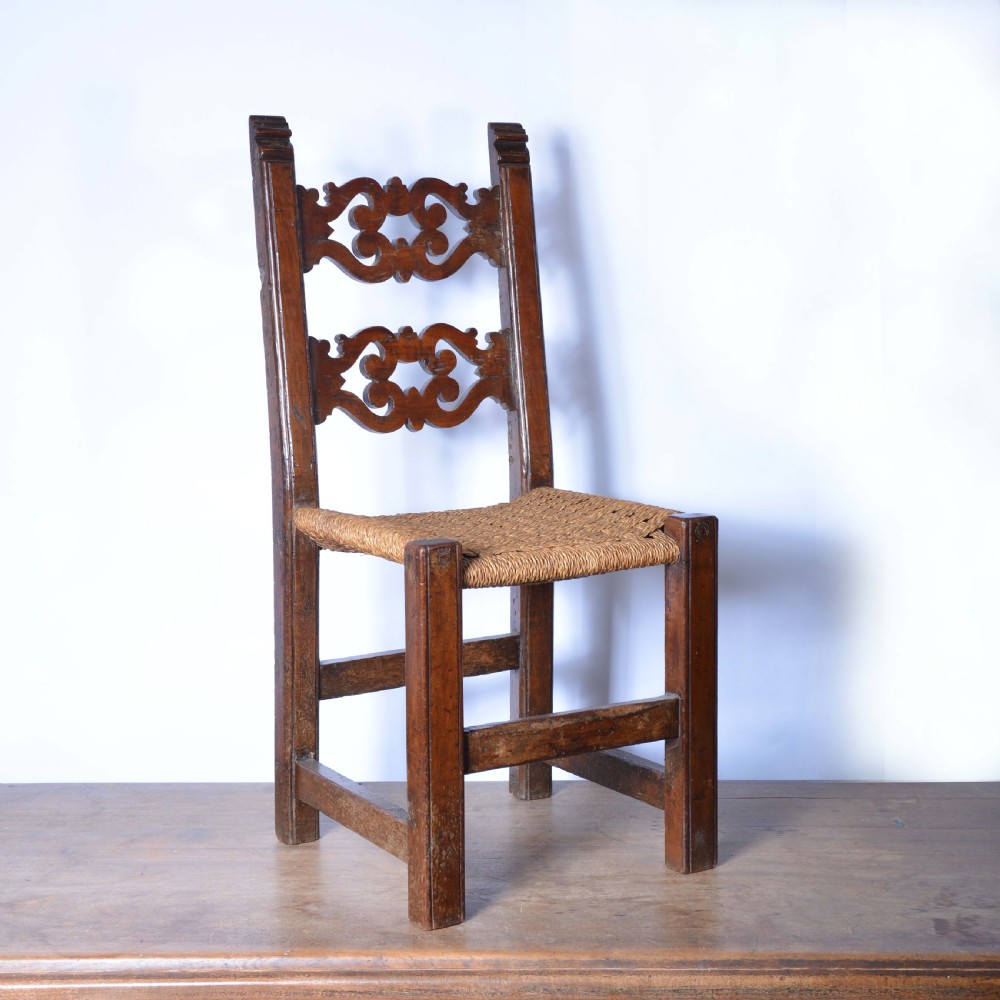 A small Italian country walnut side chair featuring two scroll-carved back splats, a woven rush seat, and sturdy square legs.