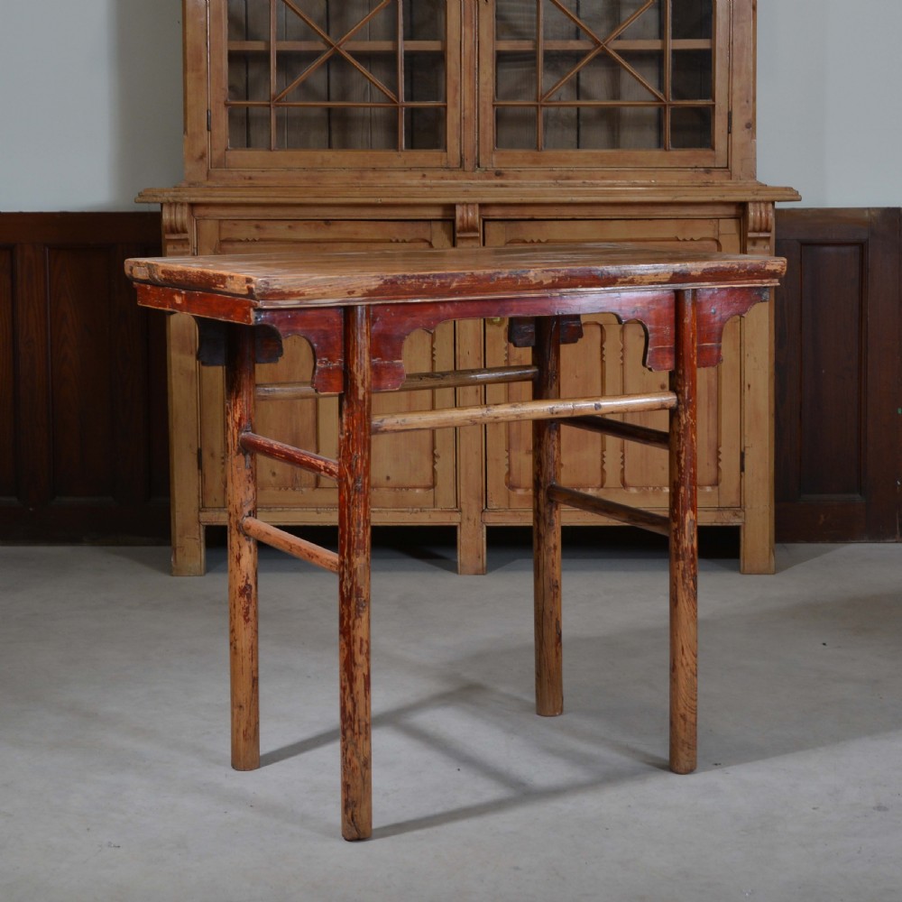 An antique Chinese rectangular elm half table featuring distressed red lacquer, carved apron spandrels, and round legs with stretchers.