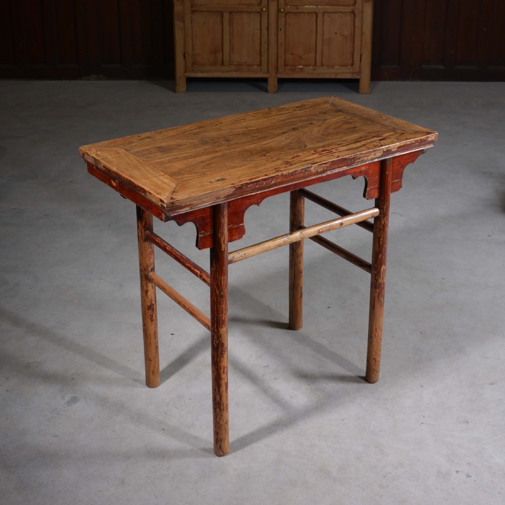 An antique Chinese rectangular elm half table featuring distressed red lacquer, carved apron spandrels, and round legs with stretchers. View II