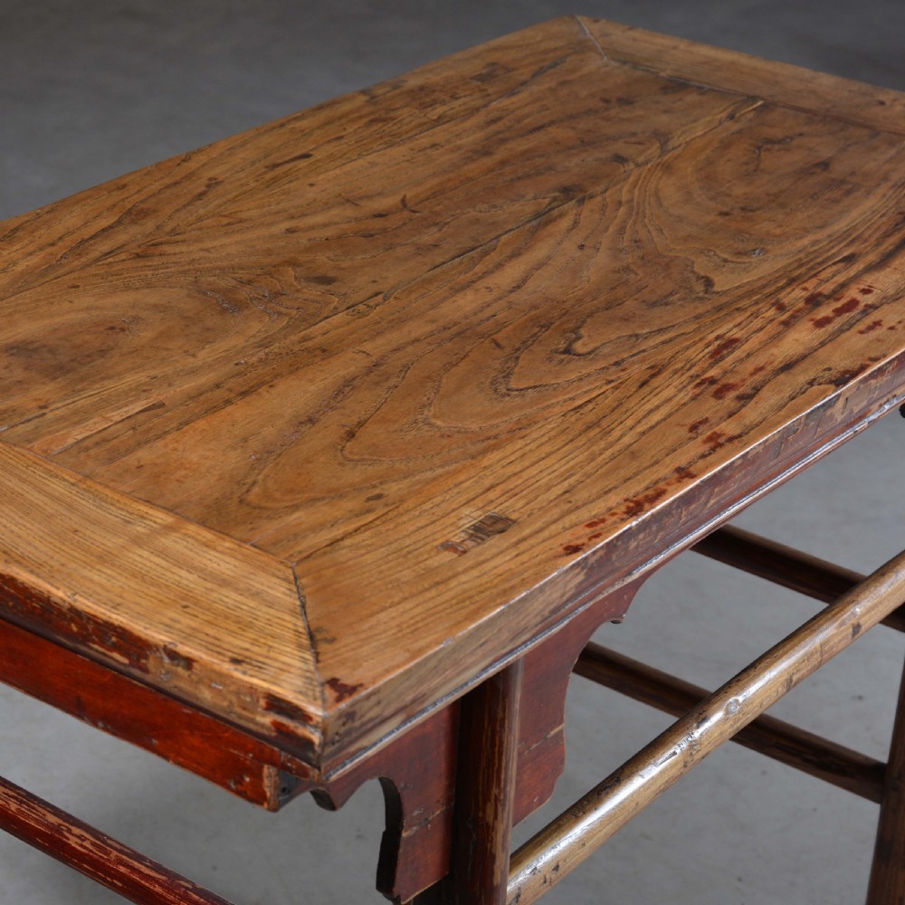 An antique Chinese rectangular elm half table featuring distressed red lacquer, carved apron spandrels, and round legs with stretchers. View V