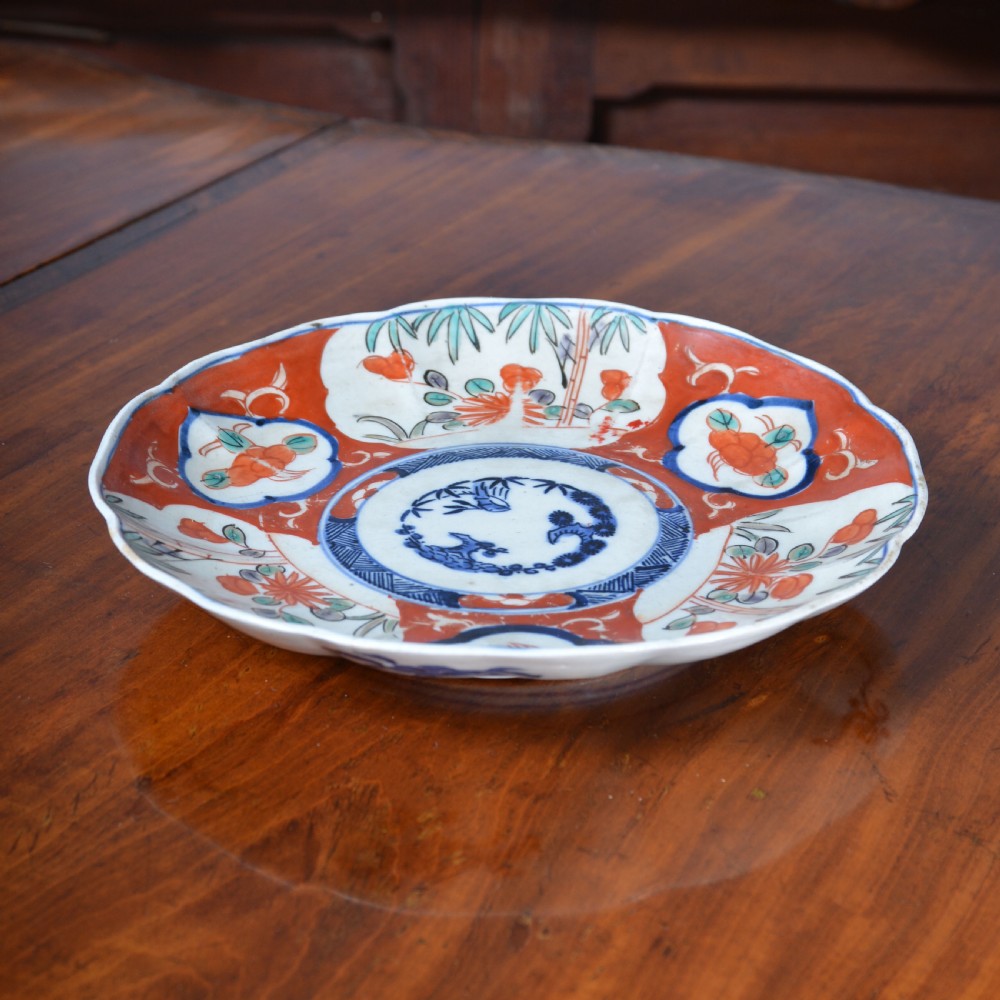 A 19th-century Japanese Imari porcelain circular dish featuring a scalloped rim, central blue medallion, and panelled floral decoration in iron red, cobalt blue, and green enamels. View II