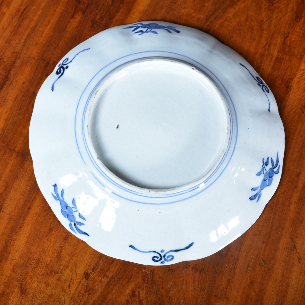 A 19th-century Japanese Imari porcelain circular dish featuring a scalloped rim, central blue medallion, and panelled floral decoration in iron red, cobalt blue, and green enamels. View VI