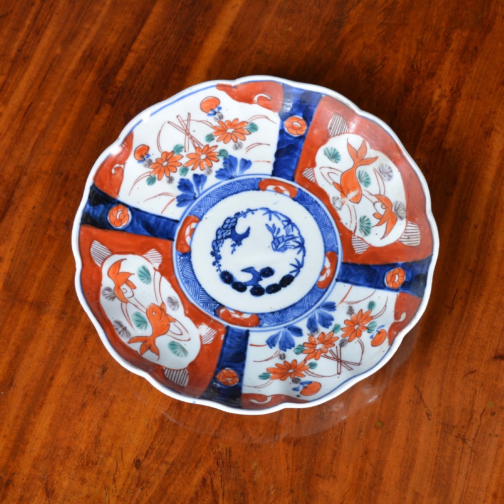 A nineteenth-century Japanese Imari porcelain plate featuring scalloped edges and hand-painted panels of goldfish and floral sprays around a circular central motif in blue and red.