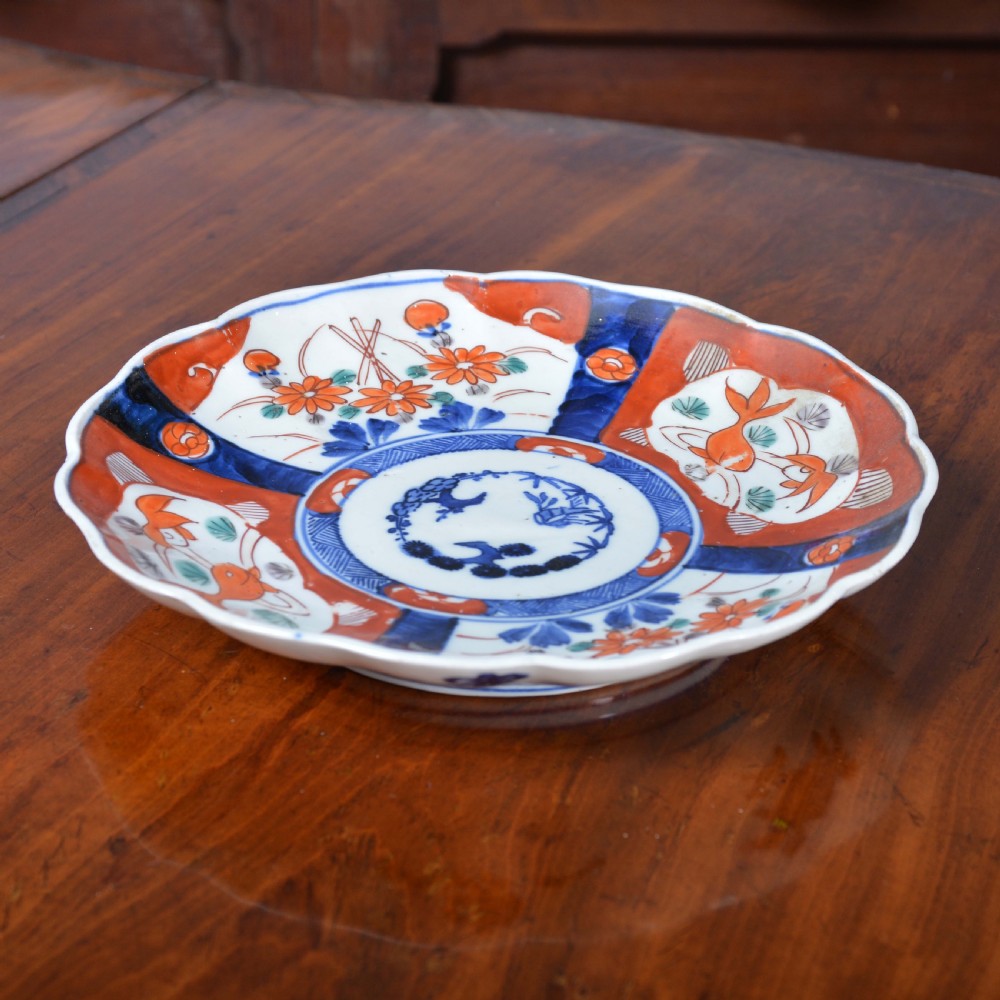 A nineteenth-century Japanese Imari porcelain plate featuring scalloped edges and hand-painted panels of goldfish and floral sprays around a circular central motif in blue and red. View II