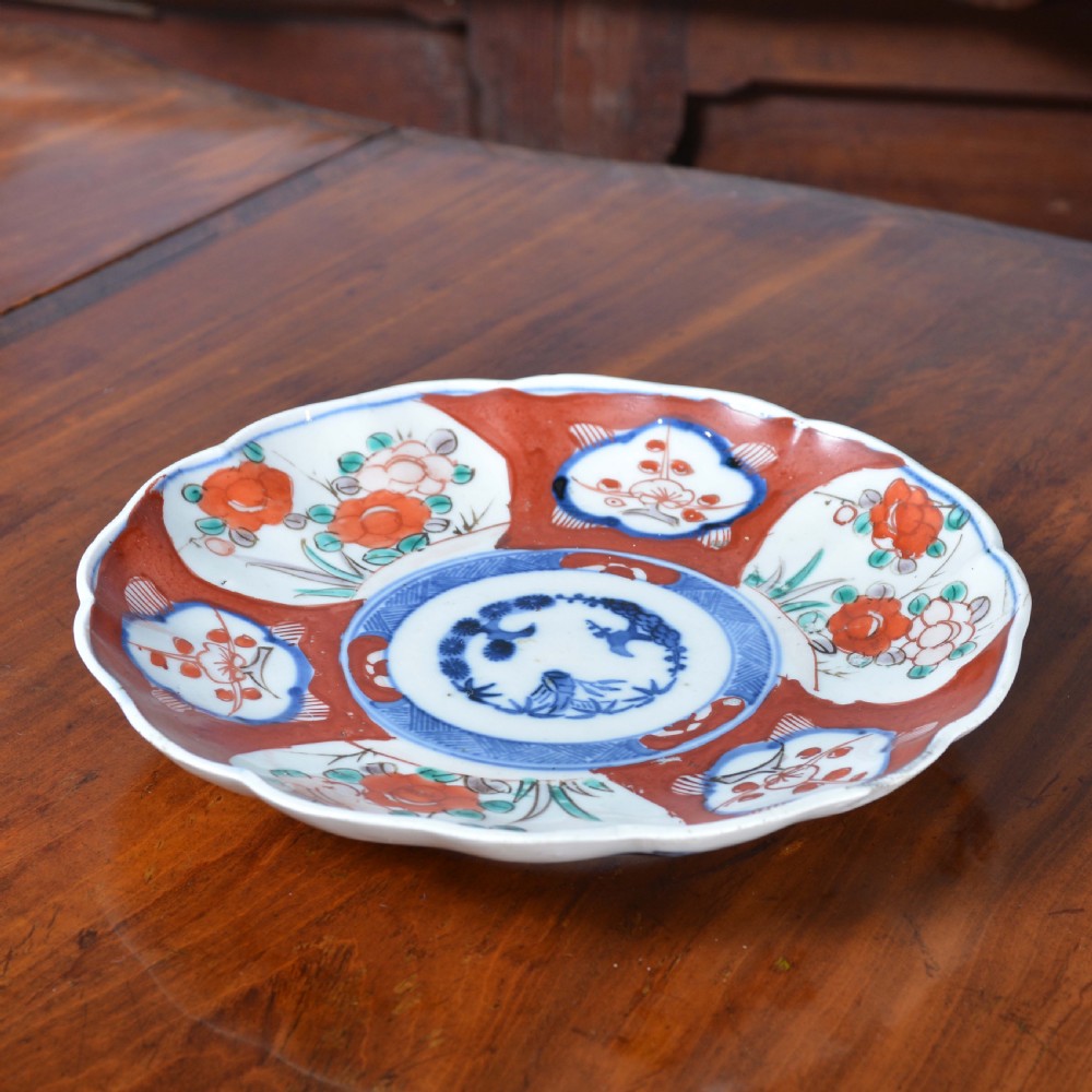 A circular 19th-century Japanese Imari porcelain plate featuring a scalloped rim, hand-painted rust-red and cobalt-blue floral motifs, and a central blue medallion. View II