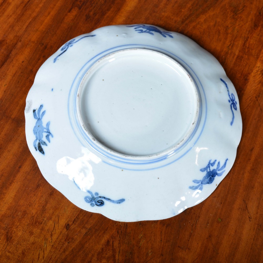 A circular 19th-century Japanese Imari porcelain plate featuring a scalloped rim, hand-painted rust-red and cobalt-blue floral motifs, and a central blue medallion. View V