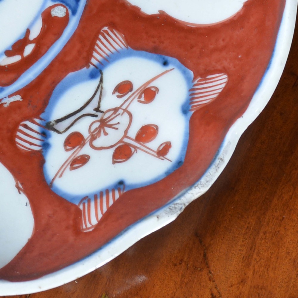 A circular 19th-century Japanese Imari porcelain plate featuring a scalloped rim, hand-painted rust-red and cobalt-blue floral motifs, and a central blue medallion. View VI