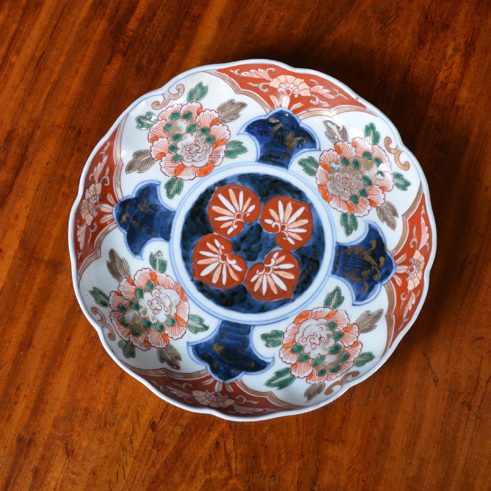 A nineteenth-century Japanese Imari porcelain plate featuring a scalloped rim, hand-painted floral motifs in iron red and green enamels, and cobalt blue brushwork with gold detailing.