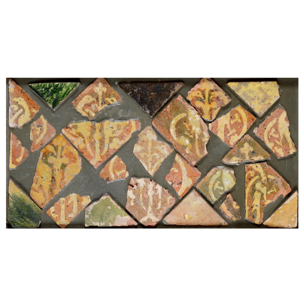 A rectangular panel displaying geometric fragments of medieval terracotta tiles with yellow slip inlaid motifs mounted in a dark backing matrix.