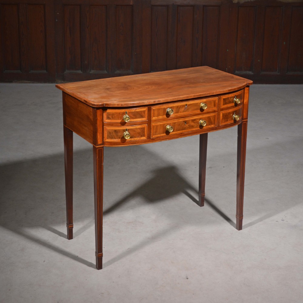 An antique Sheraton style mahogany bowfront side table with stringing inlay, brass handles, and square tapered legs. View II