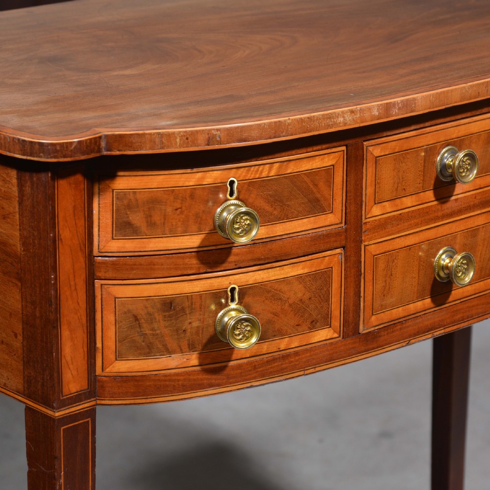 An antique Sheraton style mahogany bowfront side table with stringing inlay, brass handles, and square tapered legs. View III