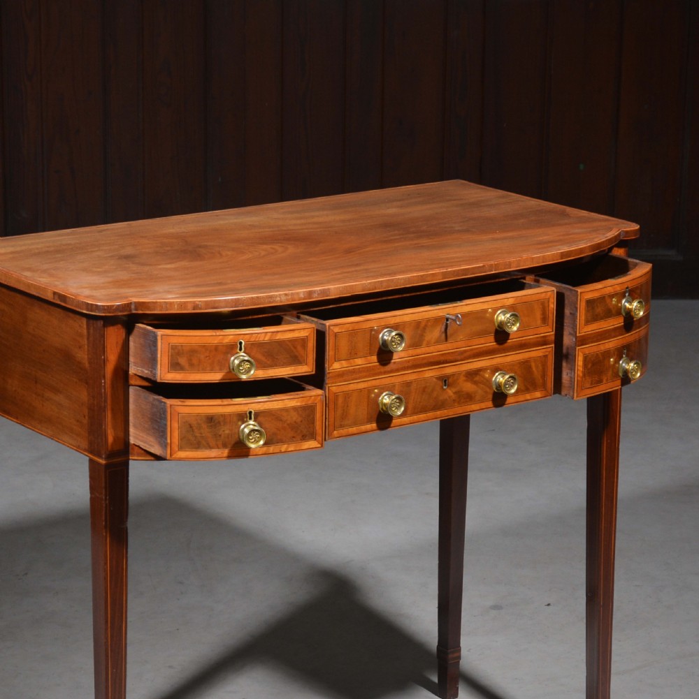 An antique Sheraton style mahogany bowfront side table with stringing inlay, brass handles, and square tapered legs. View VI