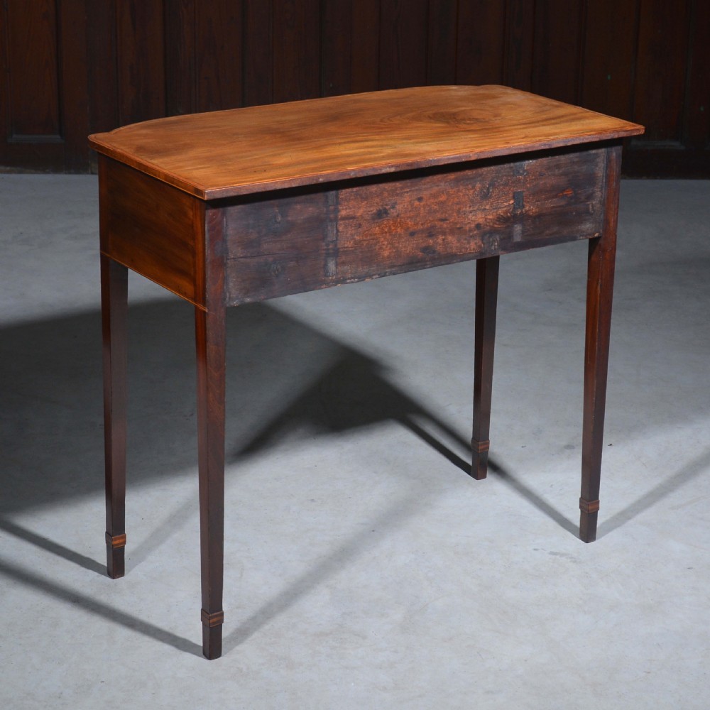 An antique Sheraton style mahogany bowfront side table with stringing inlay, brass handles, and square tapered legs. View IX