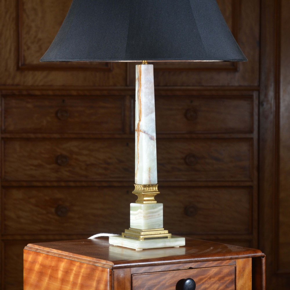 A tapered pale green onyx column table lamp featuring gilt brass collar details and a black fabric lamp shade.