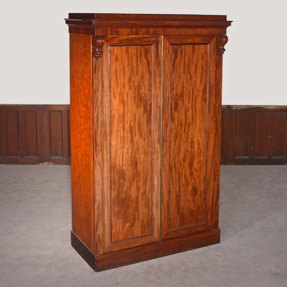 A nineteenth-century Scottish mahogany linen press featuring flame mahogany panelled doors, carved corbel brackets, and a plinth base.