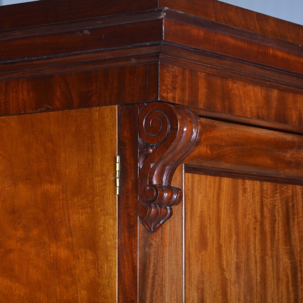 A nineteenth-century Scottish mahogany linen press featuring flame mahogany panelled doors, carved corbel brackets, and a plinth base. View II