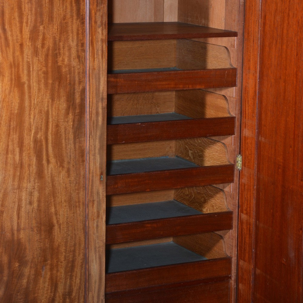 A nineteenth-century Scottish mahogany linen press featuring flame mahogany panelled doors, carved corbel brackets, and a plinth base. View VI