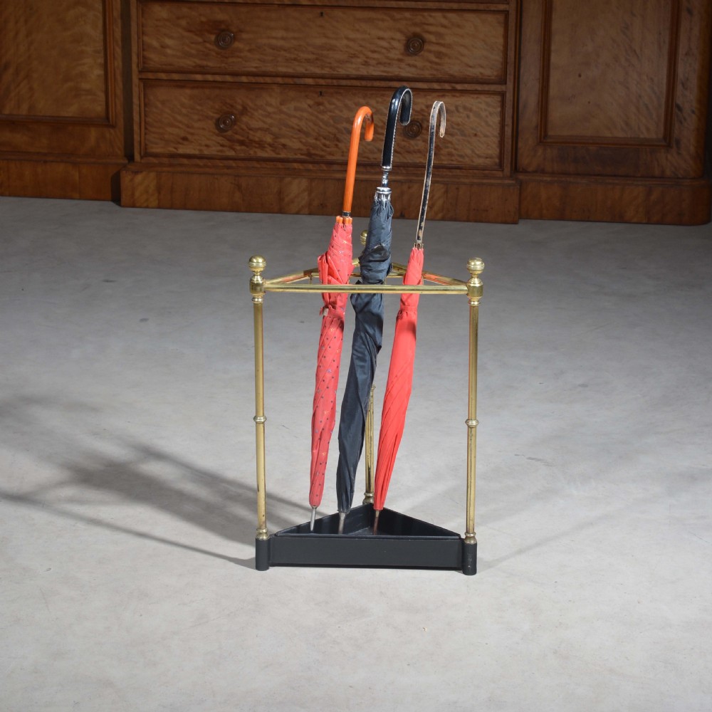 A triangular brass corner stick stand featuring tubular uprights topped with finials and a black cast iron drip tray base. View II